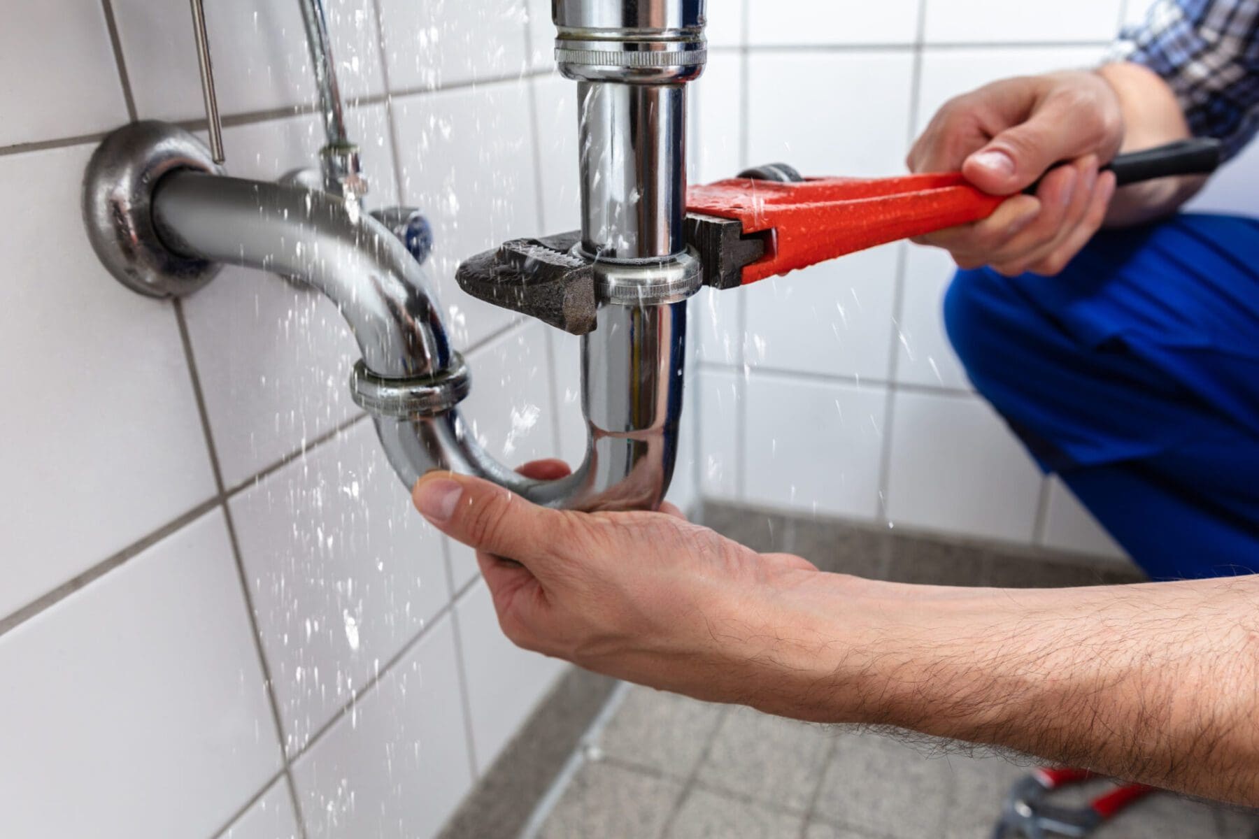 technician tightening pipes under leaking sink